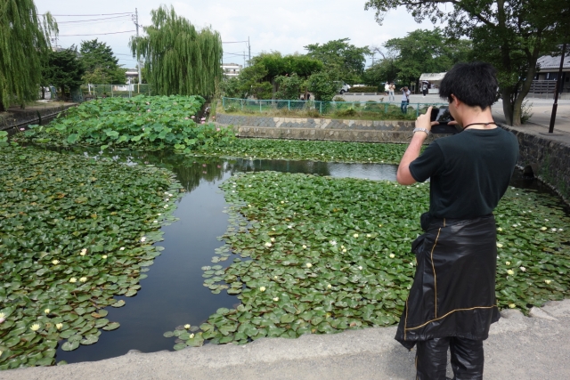 池をパチリするT氏(笑)　なんでもハスの葉の数と大きさに感動したとのこと。